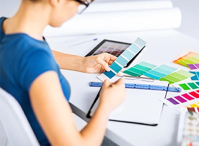 Modern ofis ortamında bir kadın çalışan, renkli tasarım kartelalarıyla karton bardak tasarımı yapıyor. Yaratıcı süreç ve ürün geliştirme ön planda.